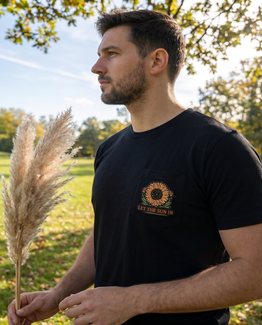 Man holding pampas grass in a field with a black t-shirt featuring a sunflower design.